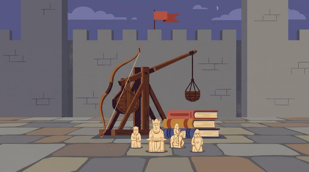 A wooden trebuchet, a recurve bow, a stack of books and a few carved chess pieces grouped together in front of a stone castle wall with a red pennant